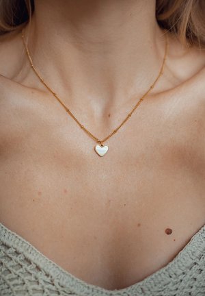Gold chain necklace with small heart pendant, featuring a polished surface. The heart shows a white interior with a gold outline.