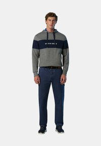Felpa grigia con striscia blu e testo "NORTH SAILS", abbinata a pantaloni blu. Design casual, in misto cotone, maniche raglan e cappuccio con lacci.