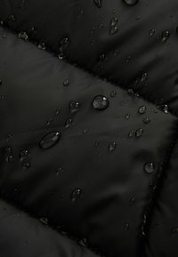 Sort stof med en quilted design, præget af vanddråber på overfladen, som fremhæver dets vandafvisende materiale.