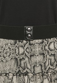 Schwarzes Oberteil mit glatter Textur, ausgestattet mit einem breiten, kontrastierenden Taillenbund und zwei silbernen Druckknöpfen. Der untere Teil hat ein Schlangenprint-Muster in Grau.