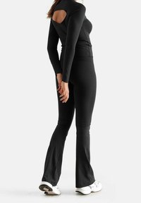 Zwarte lange mouwen top met open rugdetail, gecombineerd met zwarte flared leggings. Gladde stoftextuur, aansluitend ontwerp en sportieve stijl.