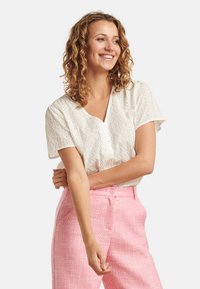 White, textured blouse with perforated patterns and short sleeves, paired with light pink, tailored trousers featuring a subtle weave.