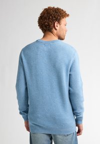 Lichtblauwe gebreide trui met een ronde halslijn, ribbels aan de mouwen en onderkant, gemaakt van een gestructureerd materiaal met fijne spikkels.