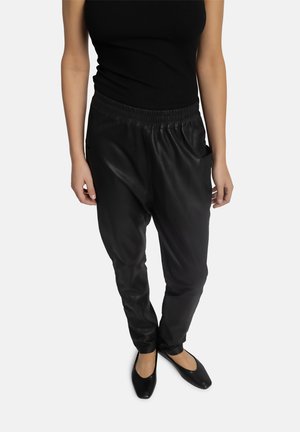 Pantalons en simili cuir noir avec taille élastique, coupe ajustée et poches latérales. Assortis avec des ballerines noires et un débardeur à côtes noir.