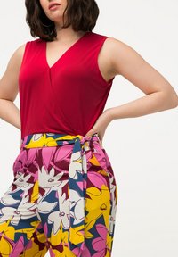 Top rosso senza maniche con scollatura a V, abbinato a pantaloni colorati con motivo floreale e cintura semitrasparente in vita.