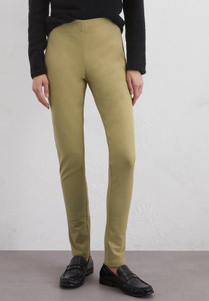Olijfgroene leggings van rekbaar materiaal, met een hoge tailleband en een aansluitend ontwerp, gecombineerd met zwarte instappers.