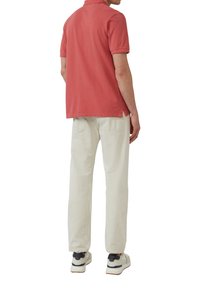 Kurzärmliges, korallenfarbenes Poloshirt mit Kragen; getragen mit cremefarbener Hose und weißen Sneakers mit dunklen Akzenten. Einfache Textur.