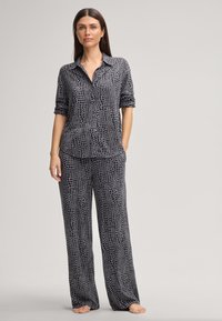 Zwart en grijs pyjama set met een overhemd met kraag en wijde broekspijpen. De stof heeft een gestructureerd krokodillenpatroon door het hele ontwerp.