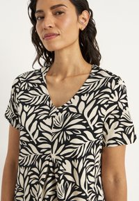 Korte mouwen V-hals top in zwart en crème met gedurfde bloemenpatronen, gemaakt van een lichtgewicht stof met een relaxte pasvorm.