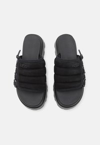 Paire de sandales noires sans lacets avec des larges sangles matelassées et un peu de détails en cordon élastique sur les côtés, vues de dessus sur fond blanc.