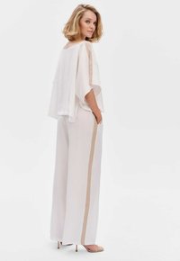 Witte, luchtige blouse met doorzichtige mouwen, gecombineerd met witte broek met wijde pijpen en een beige zijstreep. Zachte, lichtgewicht stofstructuur.