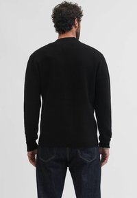 Jersey negro de punto con un acabado texturizado, cuello redondo y mangas largas, combinado con jeans de mezclilla oscuros que presentan costuras visibles en los bolsillos traseros.