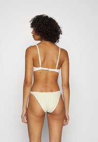 Conjunto de bikini color creme com tiras finas e um fecho nas costas. A parte de baixo apresenta riscas verticais e um design de perna alta.