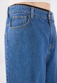 Blue denim jeans with contrasting yellow stitching, featuring a standard five-pocket design, and a straight leg cut. Soft texture.