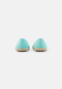 Chaussons en tissu turquoise avec un bout arrondi et une semelle en jute naturel. Design simple, texture lisse et bords fins.