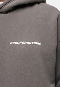Grijze hoodie met een witte tekstlogo "GOODFOR NOTHING" op de borst. Gemaakt van zacht materiaal met een ontspannen pasvorm en een verstelbare capuchon.