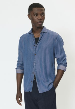 Lyseblå denimskjorte med lange, optrukne ærmer, knapper foran og en afslappet pasform, kombineret med mørke bukser med nålestriber.