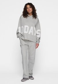 Grijze hoodie met "10 DAYS" in vetgedrukte witte letters, gecombineerd met bijpassende grijze joggingbroek. Zachte stof met een relaxte pasvorm. Draagt met grijze sneakers.
