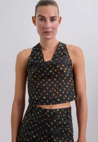 Top corto tipo halter de tela negra con un patrón geométrico colorido en verde, naranja y amarillo. Textura suave, ajuste casual.