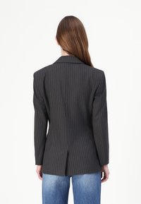 Blazer gris à rayures taillé avec des épaules structurées, fente simple à l'arrière, associé à un jean bleu clair à jambes larges.