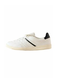 White leather sneaker with black accents, feature textured back, flat laces, and a slightly off-white rubber sole.