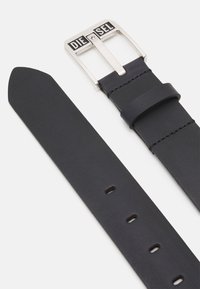 Ceinture en cuir noir avec une boucle en métal argenté. La boucle présente des lettres en relief formant le mot "DIESEL". Le cuir est lisse avec des coutures visibles.
