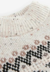 Stickad tröja med ribbat krage. Huvudfärgen är krämfärgad med prickiga accenter i bruna och svarta nyanser av geometriska mönster.