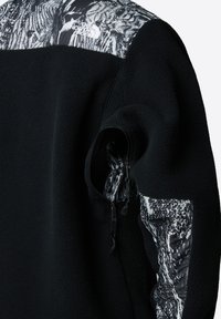 Czarna polarowa kurtka z teksturowanym korpusem, wzorzystą tkaniną na ramionach oraz zamykaną na zamek kieszenią na rękawie.