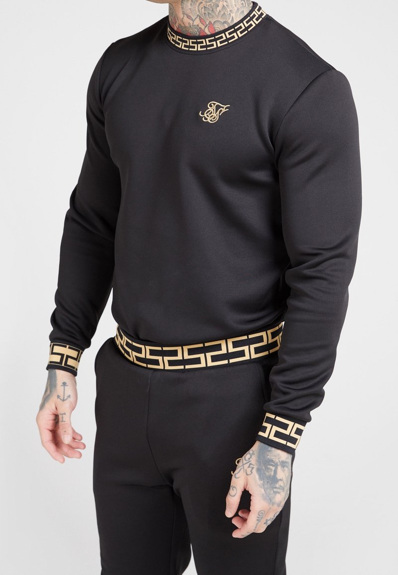 Svart atletisk sweatshirt med guldaccenter. Har ett mönstrat krage och manschetter, en snug passform och matchande midja.
