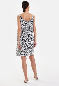 Vestido sin mangas elegante en estampado de leopardo blanco y negro, con cintura ajustada y un dobladillo ligeramente acampanado. Textura de tela suave.