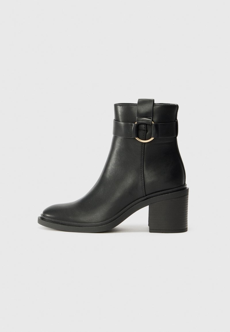 Bottine noire en cuir avec talon bloc, bout rond et lanière décorative avec boucle anneau dorée sur le côté.