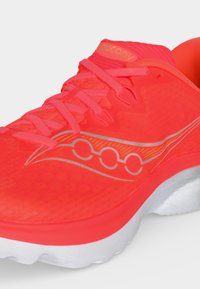 Chaussure de course athlétique rouge vif avec des lacets roses, une semelle blanche et un logo sur le côté, vue sous un angle avant latéral.