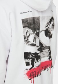 Sudadera blanca con una impresión en negro y gris de "La Creación de Adán" de Miguel Ángel, con salpicaduras de pintura roja debajo del texto.