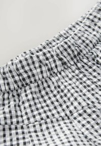 Tessuto a scacchi bianco e nero con cintura elastica arricciata, caratterizzato da un piccolo motivo a gingham e da una texture morbida.