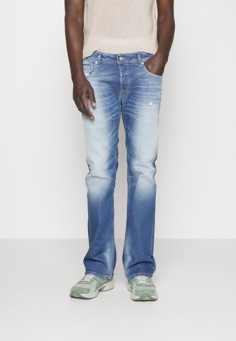 Pantalones vaqueros de mezclilla azul claro con lavado desteñido, diseño de pierna recta, cinco bolsillos y costuras en contraste. Combinados con un top de punto beige y zapatillas verdes.