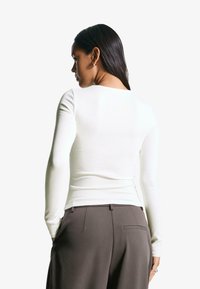 Witte longsleeve top met een ronde halslijn, gemaakt van een gladde, aangesloten stof, gecombineerd met grijze gepersonaliseerde broek.