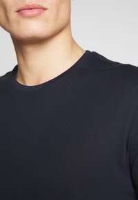 Marineblauw T-shirt met ronde hals, close-up weergave, gemaakt van soepel katoen met een aansluitend ontwerp en korte mouwen. Subtiele textuurdetails zichtbaar.