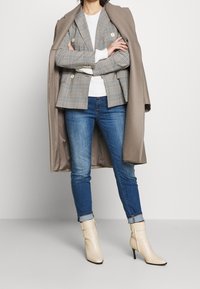 Kostkované sako v šedé a bílé barvě, vrstvené přes lehký svetr, spárované s modrými úzkými džíny a krémovými kotníkovými botami se zipovým detailem.