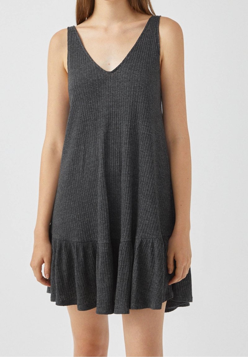 Robe sans manches en maille côtelée gris charbon avec décolleté en V et ourlet à volants portée par une personne visible des épaules jusqu'au milieu des cuisses.