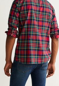 Rød og blå ternet skjorte med langeærmer, knapmanchetter og en afslappet pasform, parret med blå jeans. Stof virker tekstureret og afslappet.