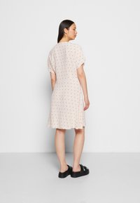 Vestido de manga curta, rosa claro, com um ajuste descontraído, apresentando um padrão de bolinhas em preto. O material é suave com uma textura lisa.