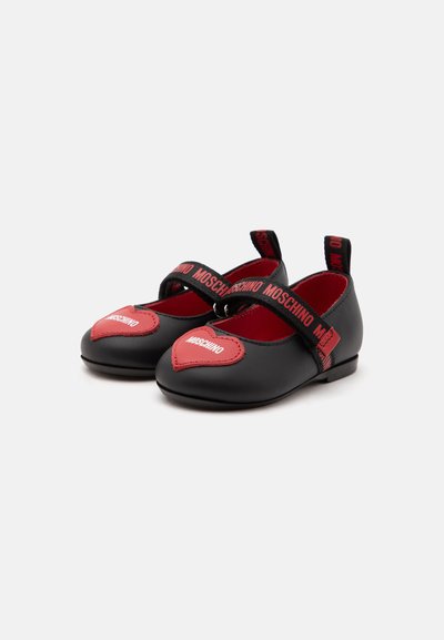 Chaussures bébé noires et rouges avec patchs en forme de cœur et sangles élastiques marquées du nom « MOSCHINO », sur fond blanc.