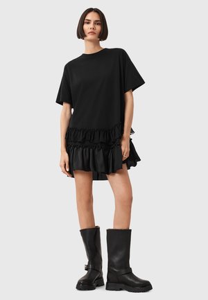 Black frilled dress with a loose fit, featuring a ruffled hem; paired with tall black leather boots with a strap detail.