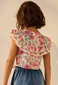 Top a fantasia floreale con bordo in pizzo arricciato, caratterizzato da uno sfondo chiaro e vivaci disegni di fiori rosa, verdi e blu.