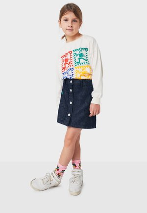 White long-sleeve shirt with colorful geometric animal graphics; dark blue corduroy skirt with front buttons; pink socks with colorful patterns; white sneakers.
