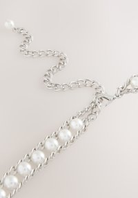 Collana con catena d'argento composta da anelli alternati a perle bianche rotonde, chiusa con un moschettone. Texture liscia e finitura lucida.