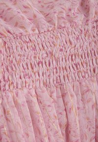 Rosa tyg med blommönster, som har samlad smockdetalj och gyllene metallaccenter. Lätt och luftig textur.