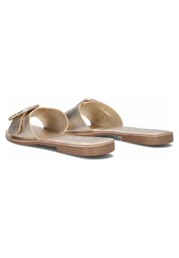 Metalen gouden slidesandalen met een gladde afwerking, brede open teen en een platte tan voetbed. Heeft een decoratieve vierkante gesp op de band.