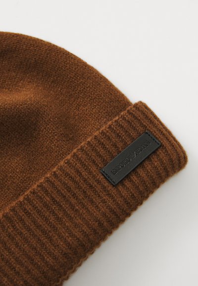 Căciulă tricotată maro cu tiv ribat. Caracterizată de un etichetă din piele neagră cu inscripția "Emporio Armani" embosată. Textură moale, design cald și confortabil.