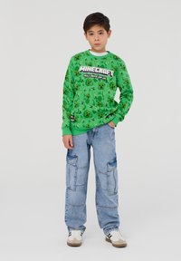 Felpa verde con motivo di Minecraft; presenta un grande logo e grafiche. Abbinata a pantaloni cargo larghi di un blu chiaro; sneakers con strisce.